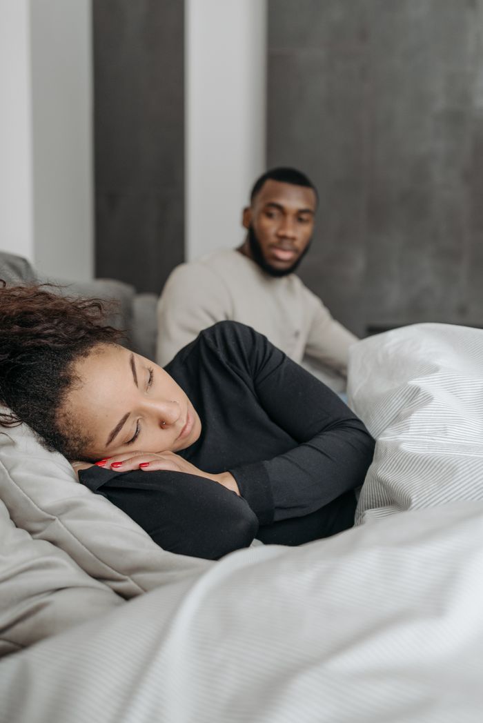 Man caring for his unwell partner resting in bed indoors, showcasing domestic support.