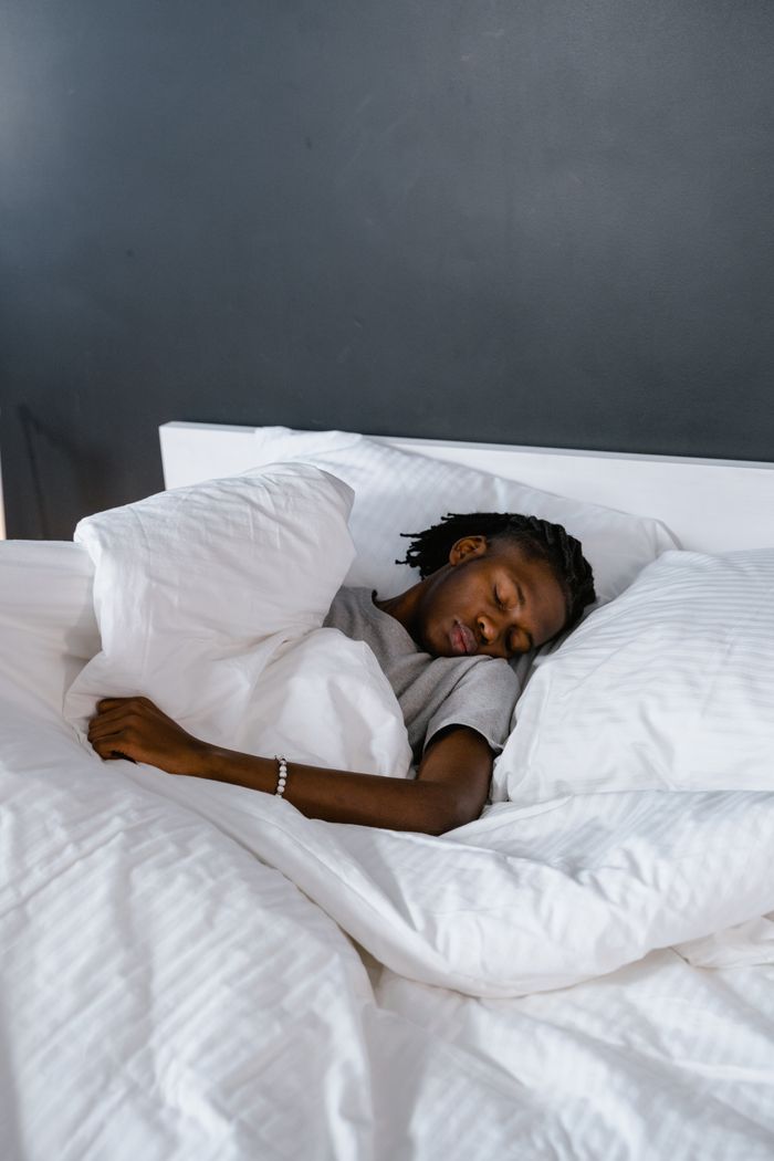 An adult sleeping peacefully on a bed with white pillows and linen.