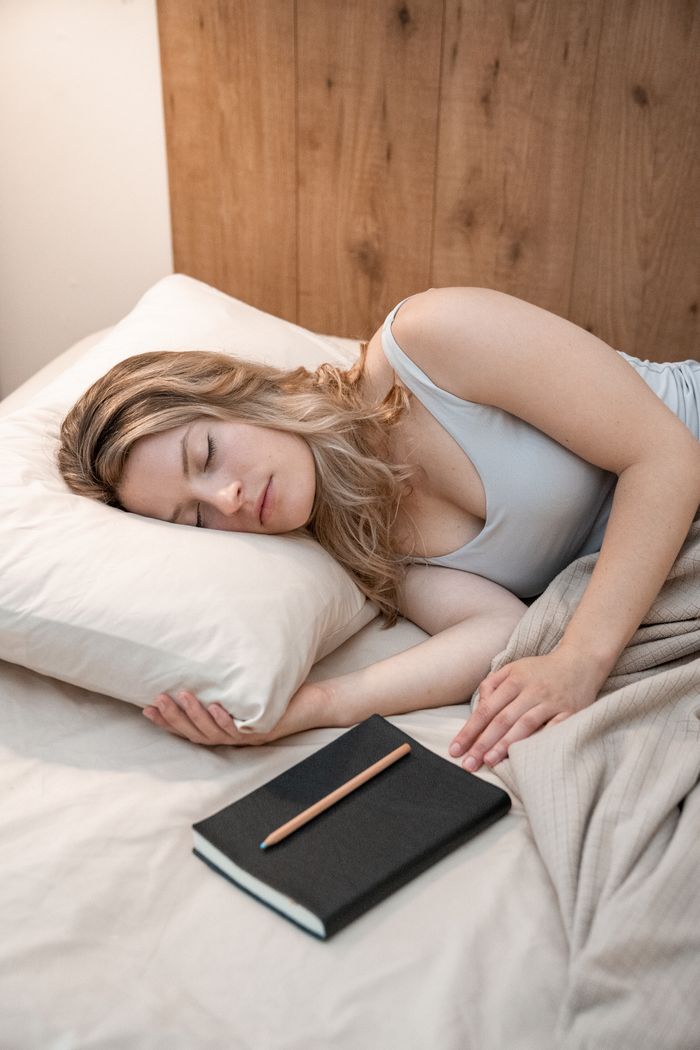 A woman peacefully sleeping in bed with a notebook and pencil, creating a serene bedtime scene.